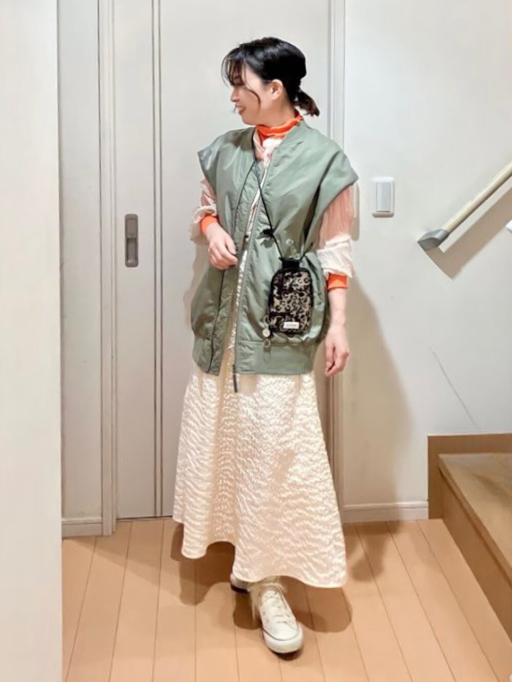 グリーン系のダウンベスト、ベージュ系のシャツ/ブラウス、オレンジ系のトップスを着用したレディースの春コーディネートの2枚目の写真