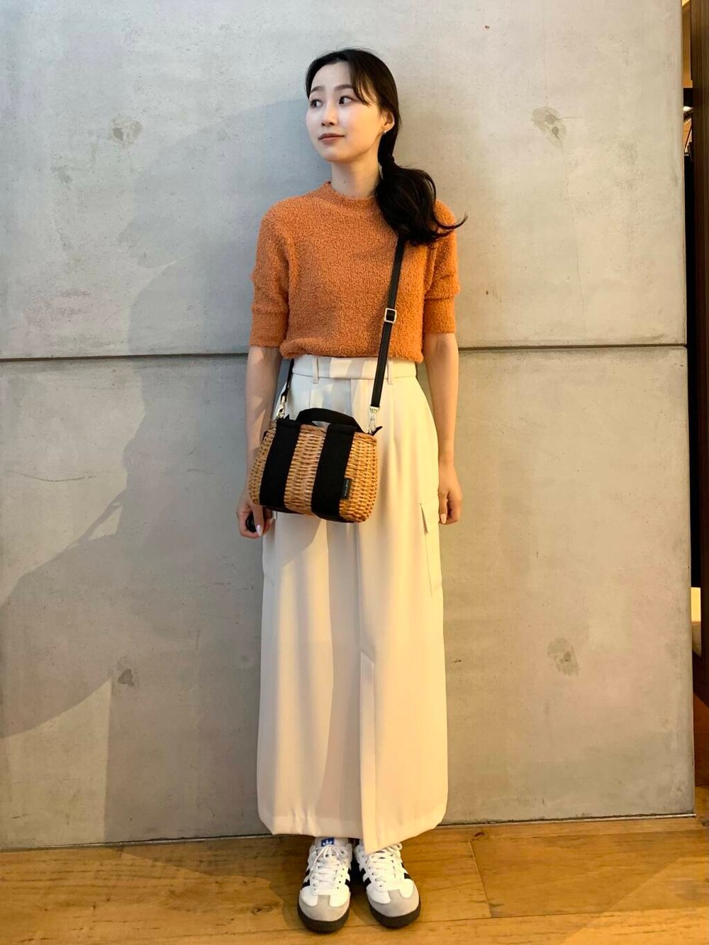 ブラック系のハンドバッグ、ホワイト系のスニーカー、オレンジ系のニット/セーターを着用したレディースの夏コーディネートの4枚目の写真