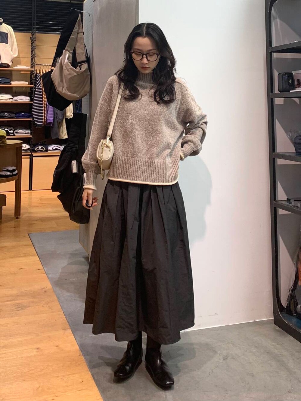 グレー系のスカート、ベージュ系のニット/セーター、ブラック系のブーツを着用したレディースの冬コーディネートの2枚目の写真