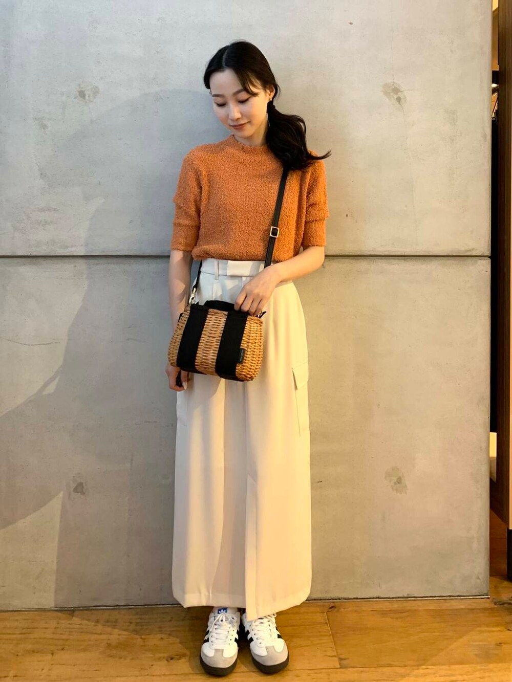 ブラック系のハンドバッグ、ホワイト系のスニーカー、オレンジ系のニット/セーターを着用したレディースの夏コーディネートの2枚目の写真
