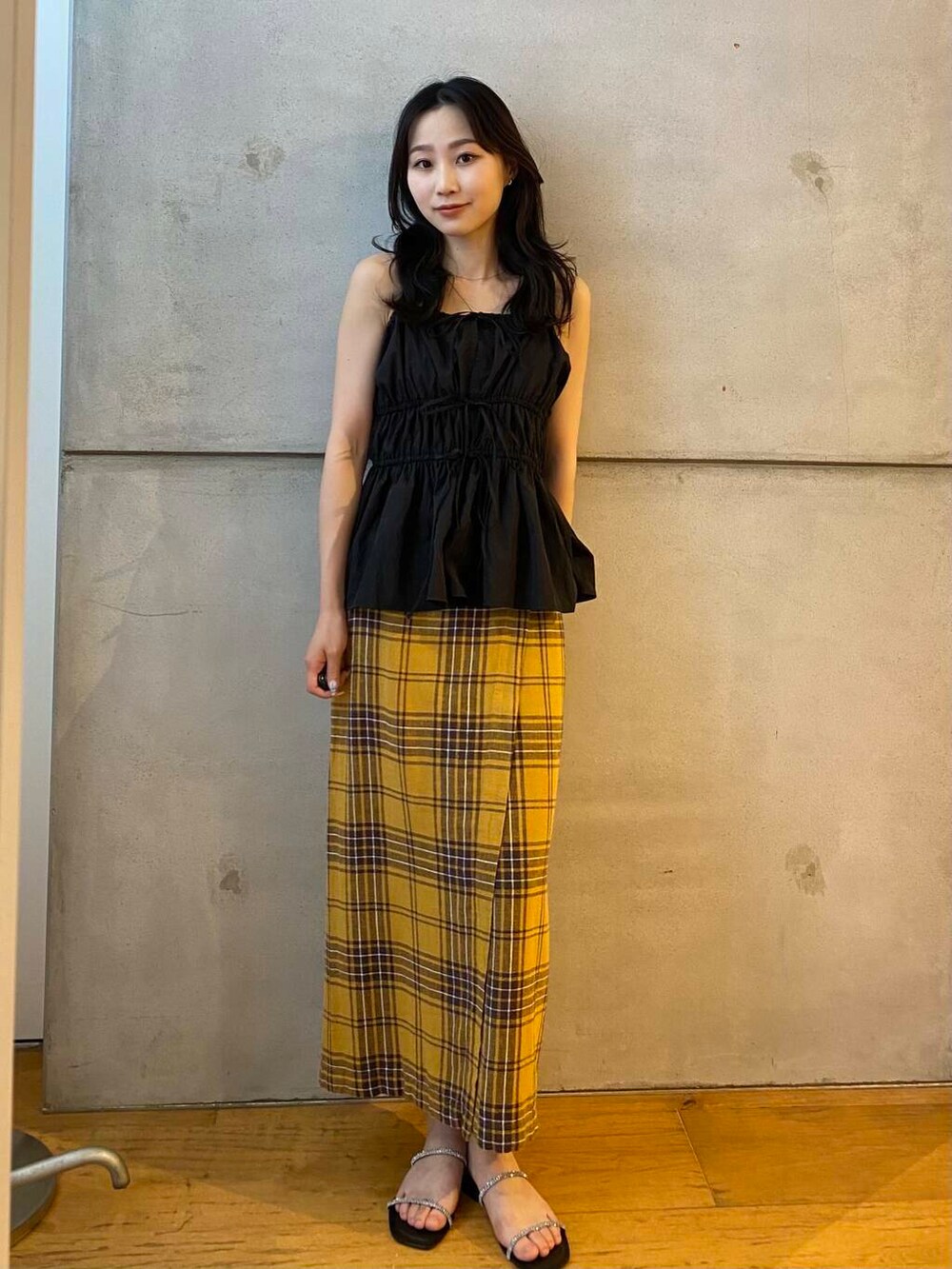 イエロー系のスカート、ブラック系のベスト、ブラック系のサンダルを着用したレディースの夏コーディネートの2枚目の写真