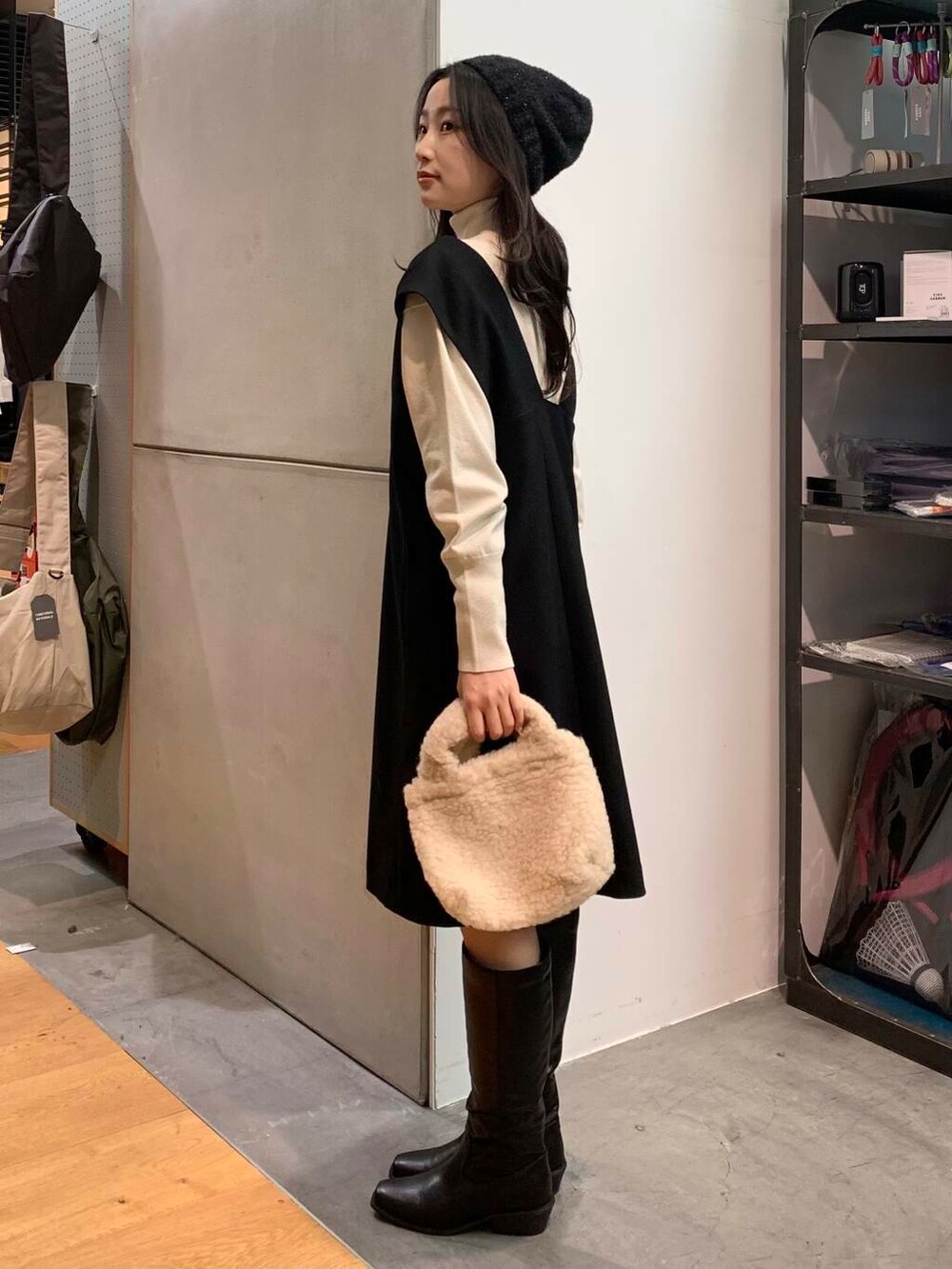 ブラック系のブーツ、ベージュ系のハンドバッグ、ブラック系のワンピースを着用したレディースの冬コーディネートの6枚目の写真