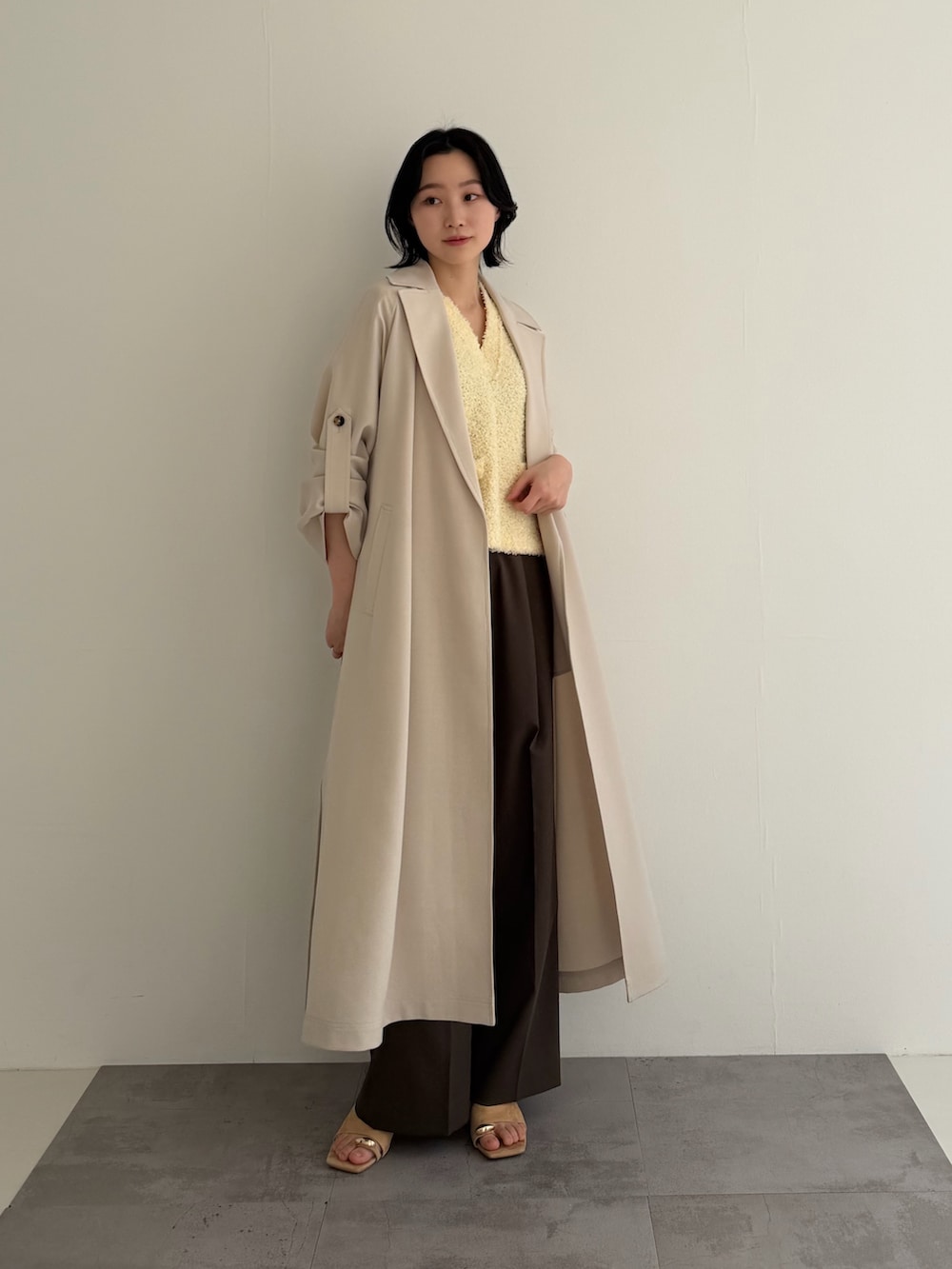 ホワイト系のトレンチコート、イエロー系のベスト、ブラウン系のその他パンツを着用したレディースの冬コーディネートの2枚目の写真