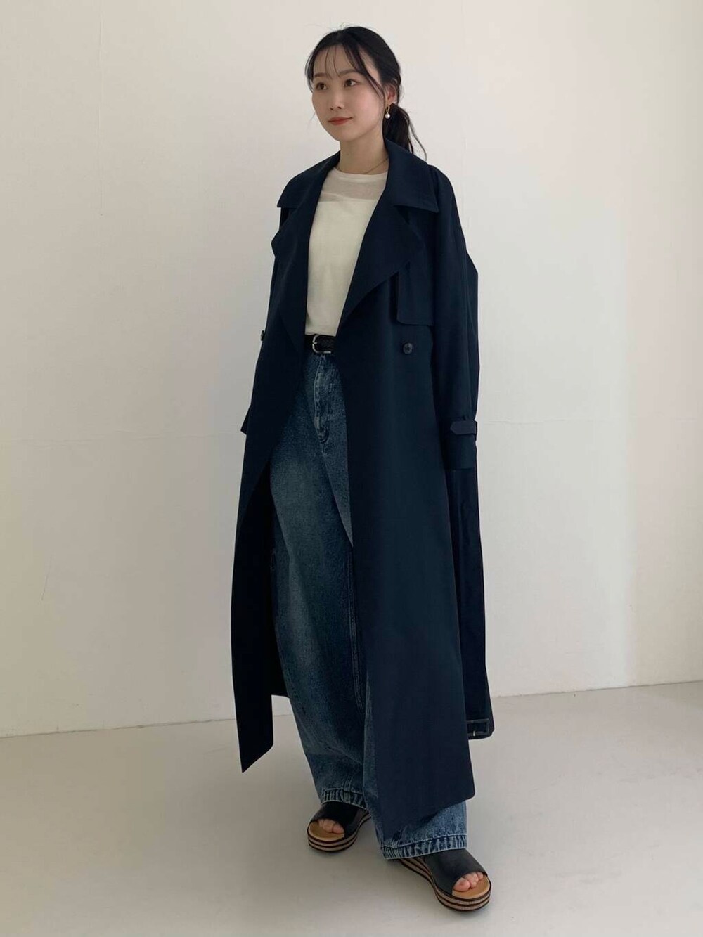 ブルー系のトレンチコート、ブルー系のデニムパンツ、ホワイト系のTシャツ/カットソーを着用したレディースの春コーディネートの2枚目の写真