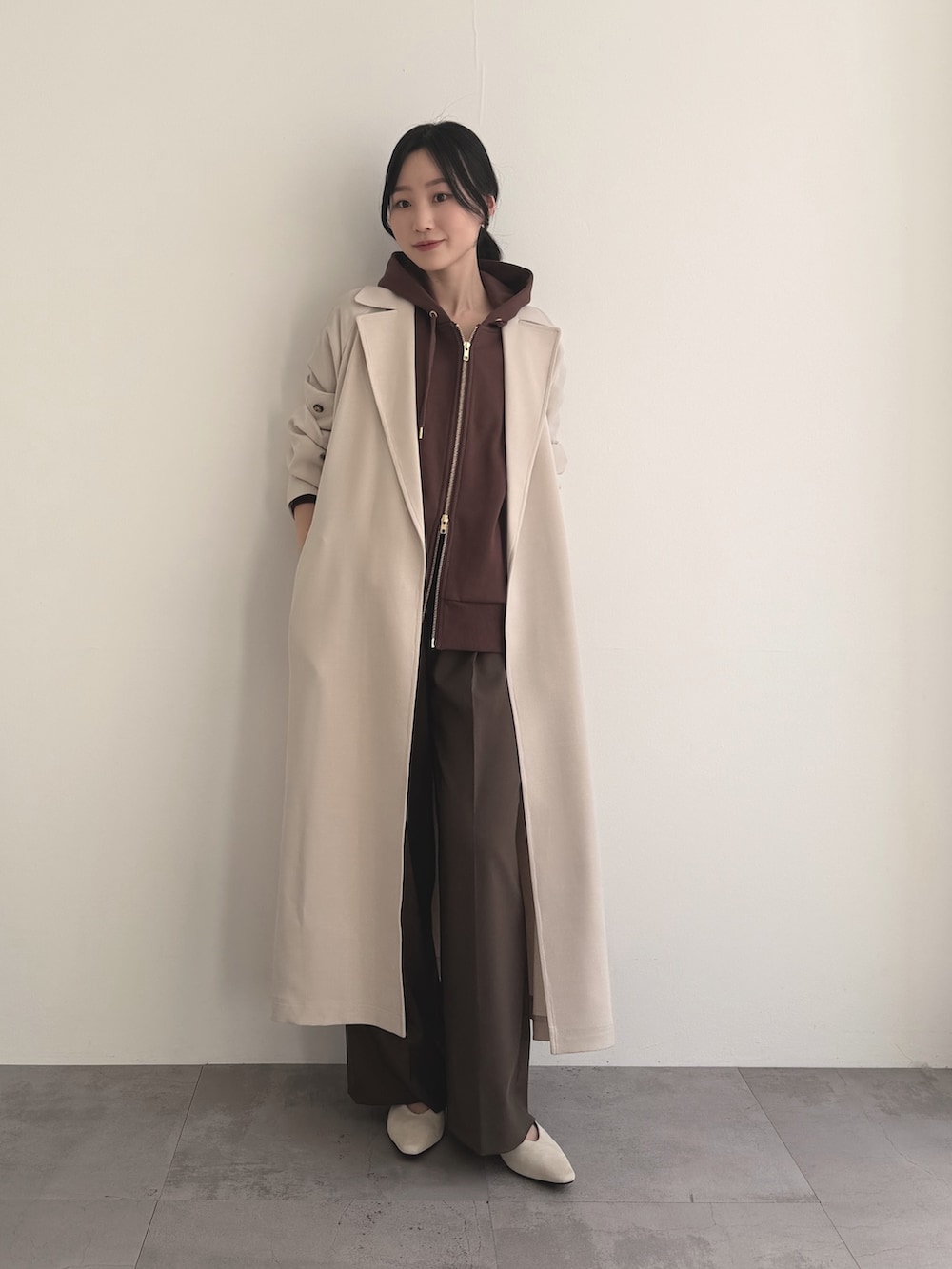 ベージュ系のトレンチコート、ブラウン系のパーカー、ブラウン系のその他パンツを着用したレディースの春コーディネートの2枚目の写真