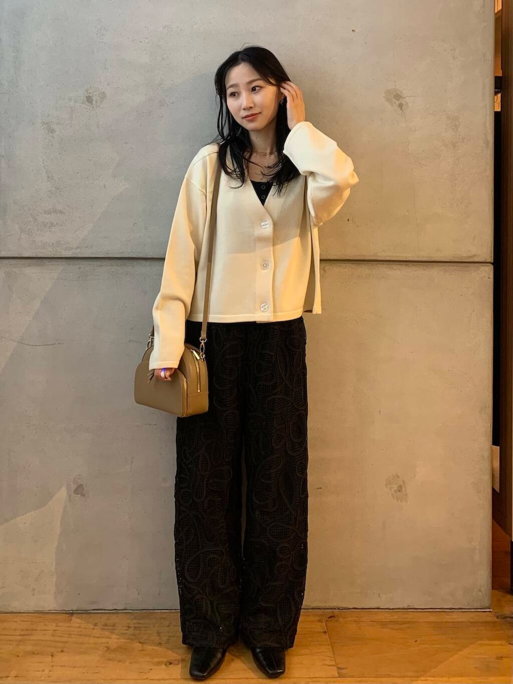ベージュ系のショルダーバッグ、ホワイト系のカーディガン/ボレロ、ブラック系のブーツを着用したレディースの秋コーディネートの2枚目の写真