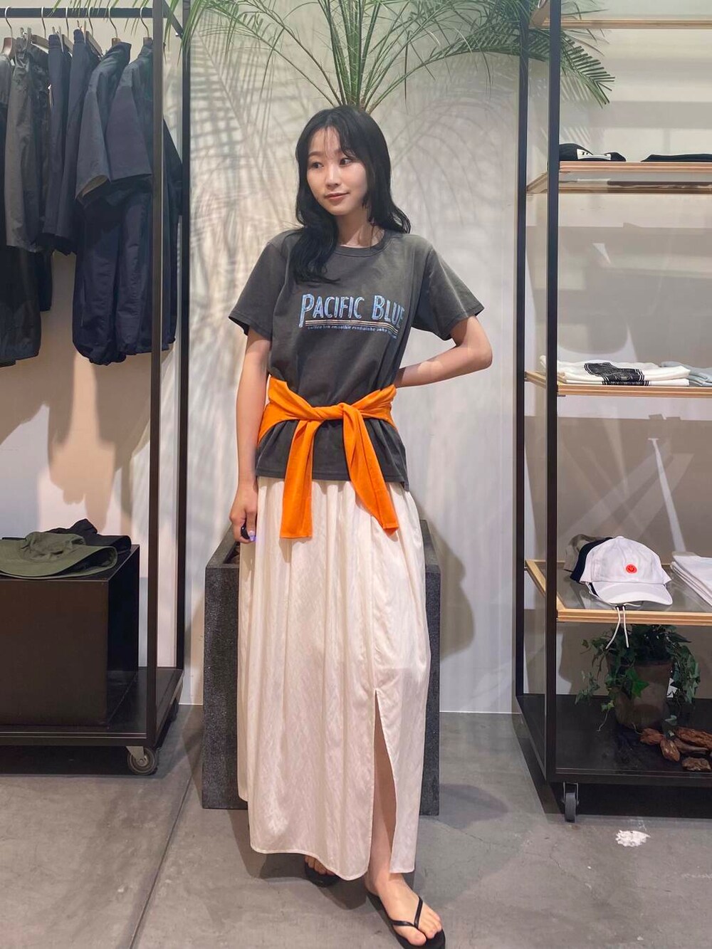 ブラック系のサンダル、オレンジ系のカーディガン/ボレロ、ホワイト系のスカートを着用したレディースの夏コーディネートの2枚目の写真