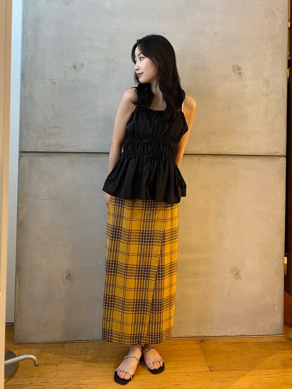 イエロー系のスカート、ブラック系のベスト、ブラック系のサンダルを着用したレディースの夏コーディネートの4枚目の写真