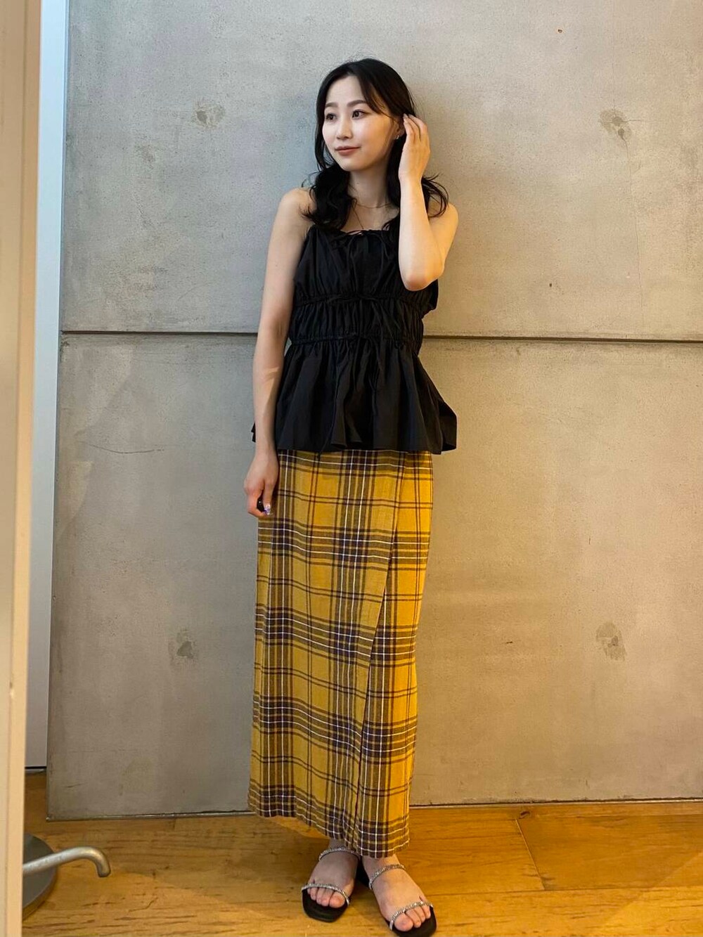 イエロー系のスカート、ブラック系のベスト、ブラック系のサンダルを着用したレディースの夏コーディネートの3枚目の写真