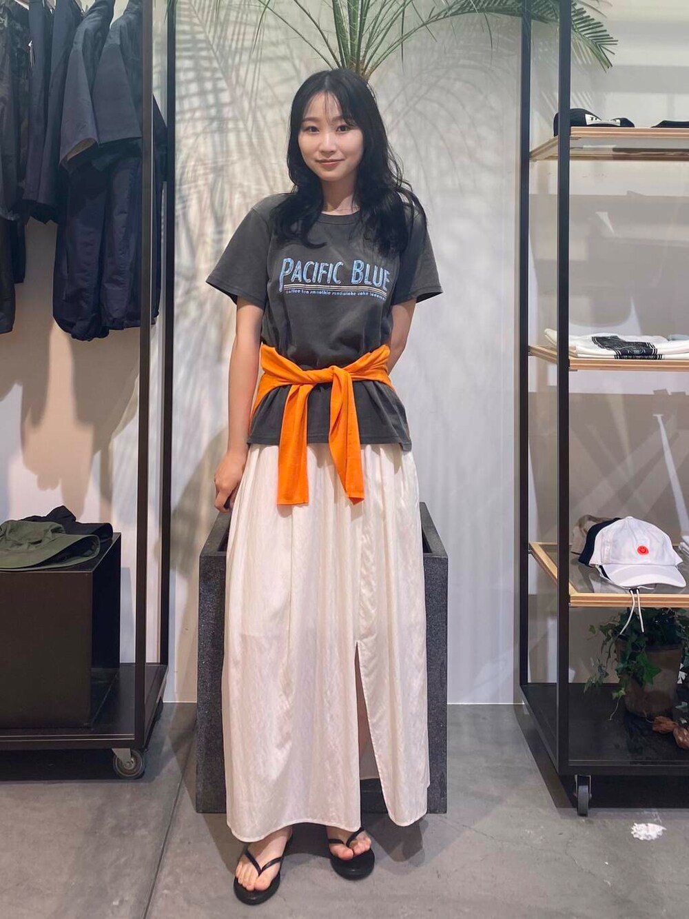 ブラック系のサンダル、オレンジ系のカーディガン/ボレロ、ホワイト系のスカートを着用したレディースの夏コーディネートの3枚目の写真