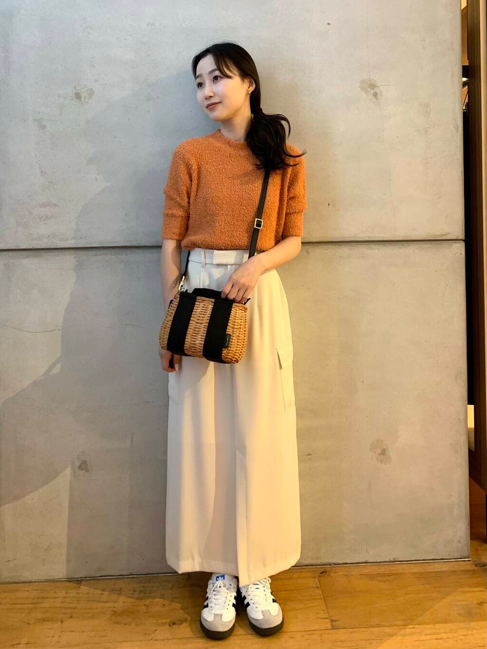 ブラック系のハンドバッグ、ホワイト系のスニーカー、オレンジ系のニット/セーターを着用したレディースの夏コーディネートの3枚目の写真