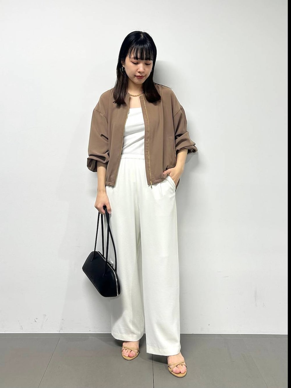 ホワイト系のスラックス、イエロー系のブルゾン、ブラック系のハンドバッグを着用したレディースの春コーディネートの2枚目の写真