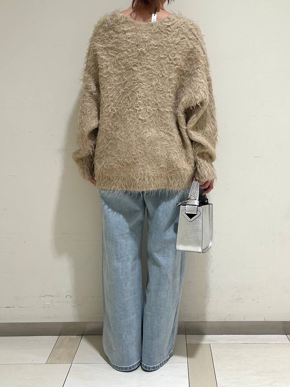 シルバー系のハンドバッグ、シルバー系のローファー、ブルー系のデニムパンツを着用したレディースの冬コーディネートの3枚目の写真