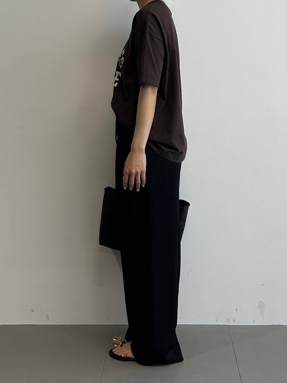 ブラック系のトートバッグ、ブラック系のサンダル、ブラウン系のTシャツ/カットソーを着用したレディースの夏コーディネートの2枚目の写真