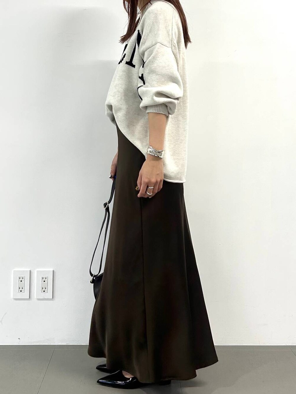 ベージュ系のニット/セーター、ブラック系のショルダーバッグ、ブラウン系のスカートを着用したレディースの冬コーディネートの2枚目の写真