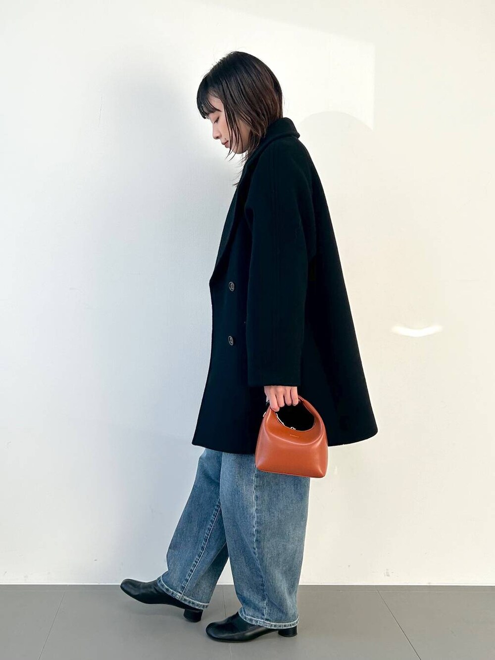 ブラウン系のショルダーバッグ、ブルー系のデニムパンツ、グレー系のニット/セーターを着用したレディースの秋コーディネートの2枚目の写真