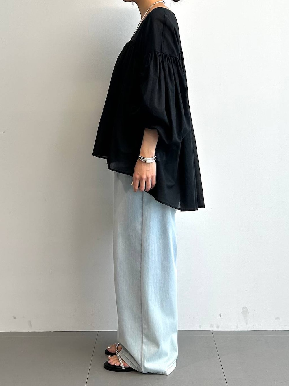 シルバー系のハンドバッグ、ブルー系のデニムパンツ、ブラック系のサンダルを着用したレディースの夏コーディネートの2枚目の写真