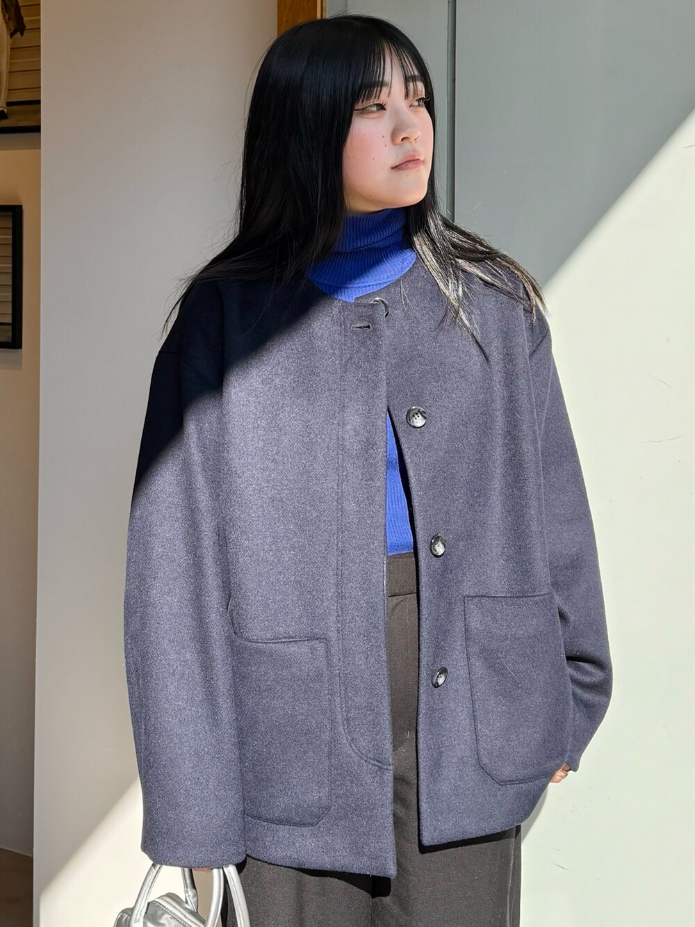 ブルー系のノーカラーコート、ブラック系のその他パンツ、シルバー系のハンドバッグを着用したレディースの冬コーディネートの4枚目の写真