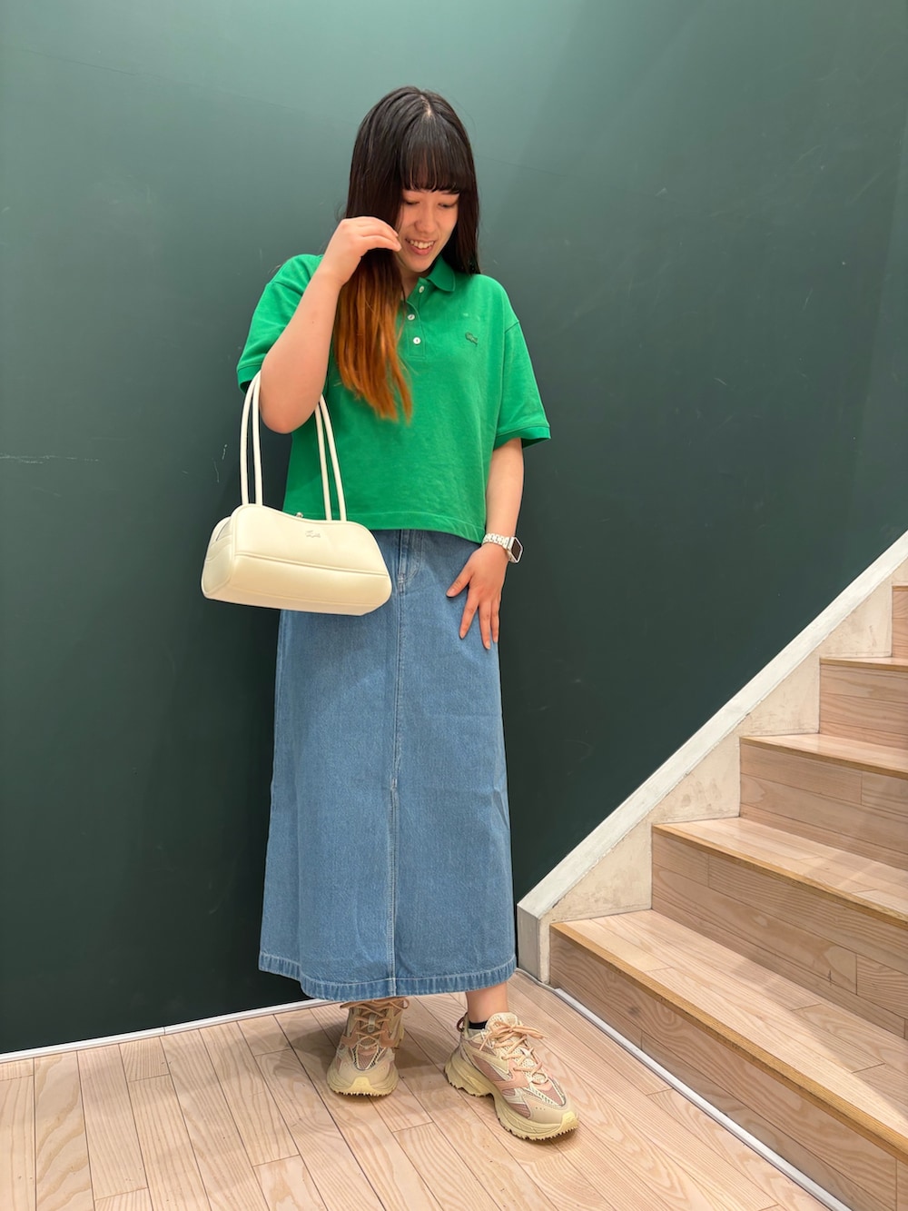 グリーン系のポロシャツ、ブルー系のデニムスカート、ホワイト系のショルダーバッグを着用したレディースの春コーディネートの2枚目の写真