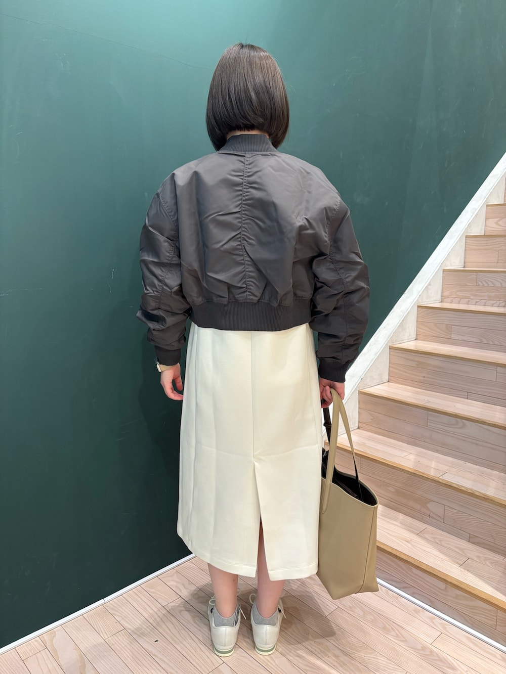 グレー系のブルゾン、ホワイト系のワンピース、ベージュ系のトートバッグを着用したレディースの冬コーディネートの2枚目の写真