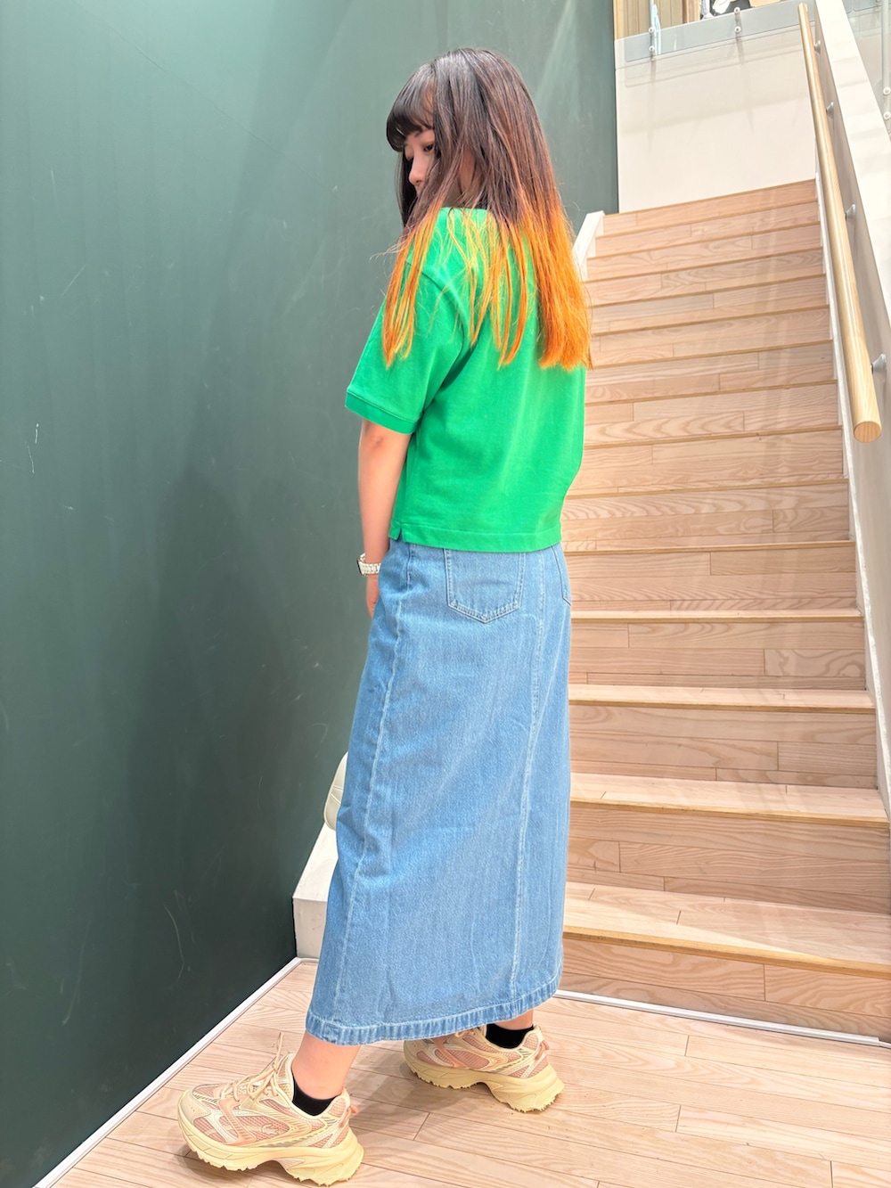 グリーン系のポロシャツ、ブルー系のデニムスカート、ホワイト系のショルダーバッグを着用したレディースの春コーディネートの3枚目の写真