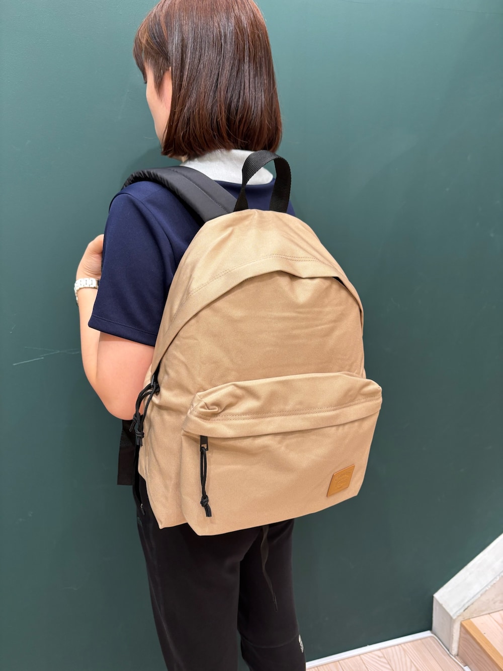 ブルー系のポロシャツ、ベージュ系のバックパック/リュック、ブラック系のスウェットパンツを着用したレディースの夏コーディネートの5枚目の写真