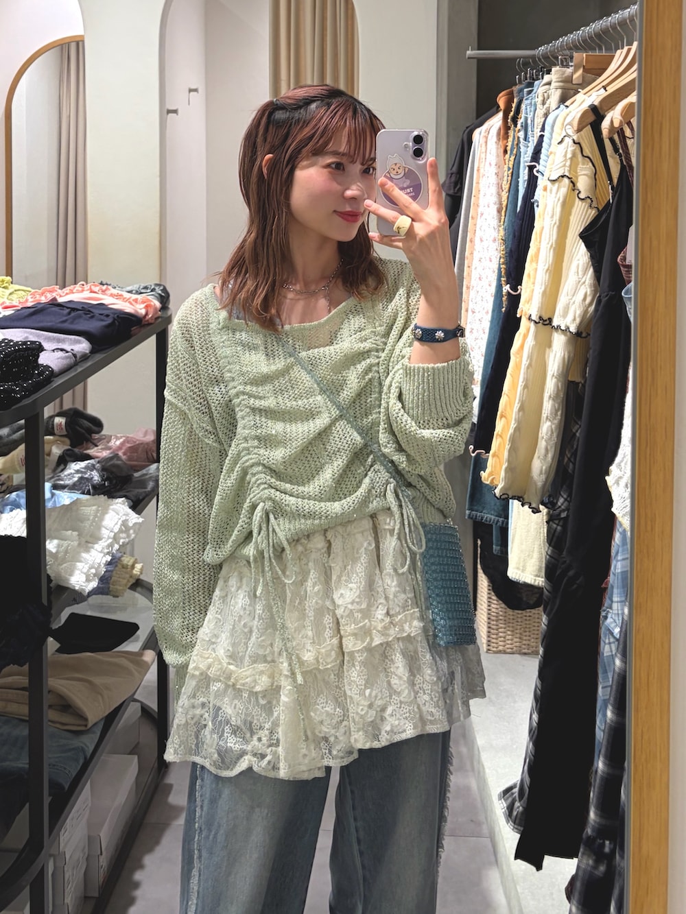 グリーン系のニット/セーター、ホワイト系のワンピース、ブルー系のデニムパンツを着用したレディースの春コーディネートの3枚目の写真