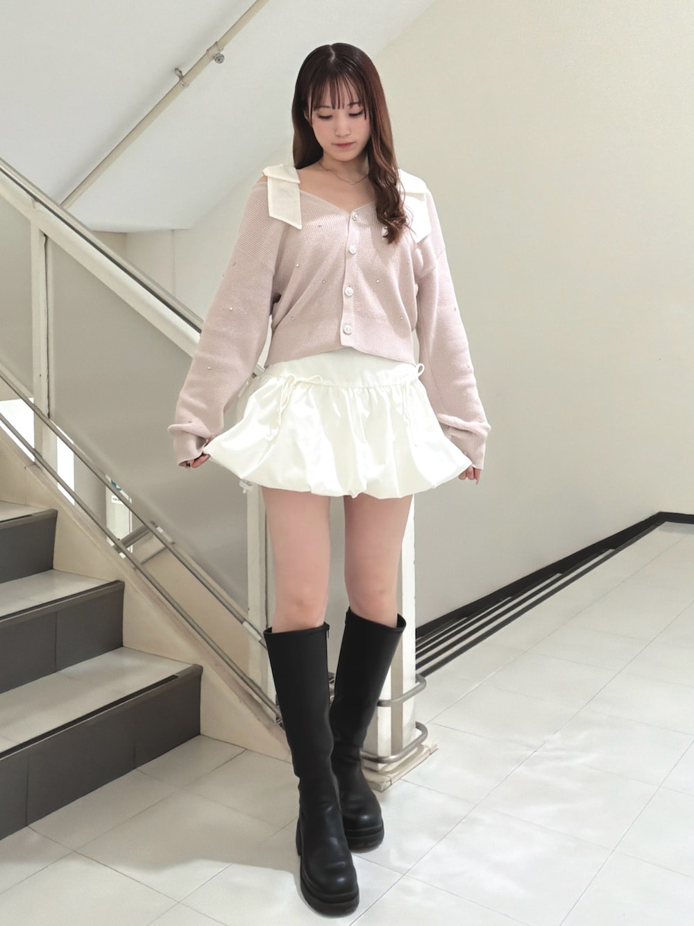 ピンク系のカーディガン/ボレロ、ホワイト系のスカート、ブラック系のブーツを着用したレディースの冬コーディネートの3枚目の写真