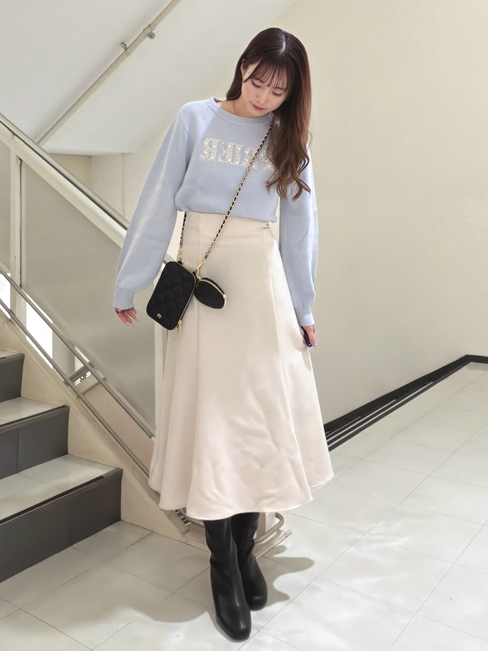 ブルー系のニット/セーター、ブラック系のショルダーバッグ、ベージュ系のスカートを着用したレディースの冬コーディネートの2枚目の写真