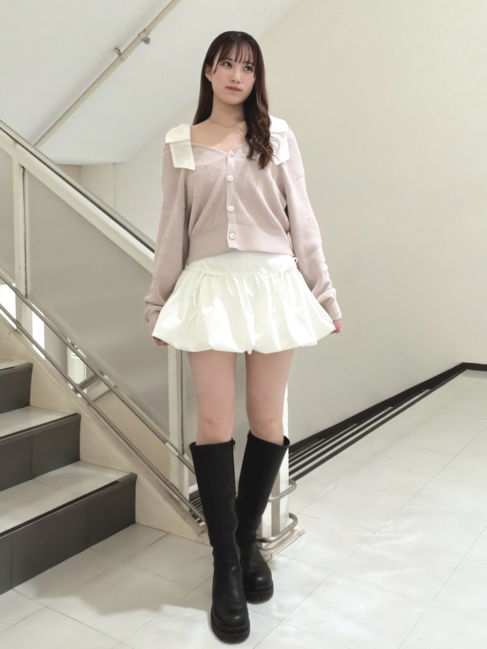 ピンク系のカーディガン/ボレロ、ホワイト系のスカート、ブラック系のブーツを着用したレディースの冬コーディネートの2枚目の写真