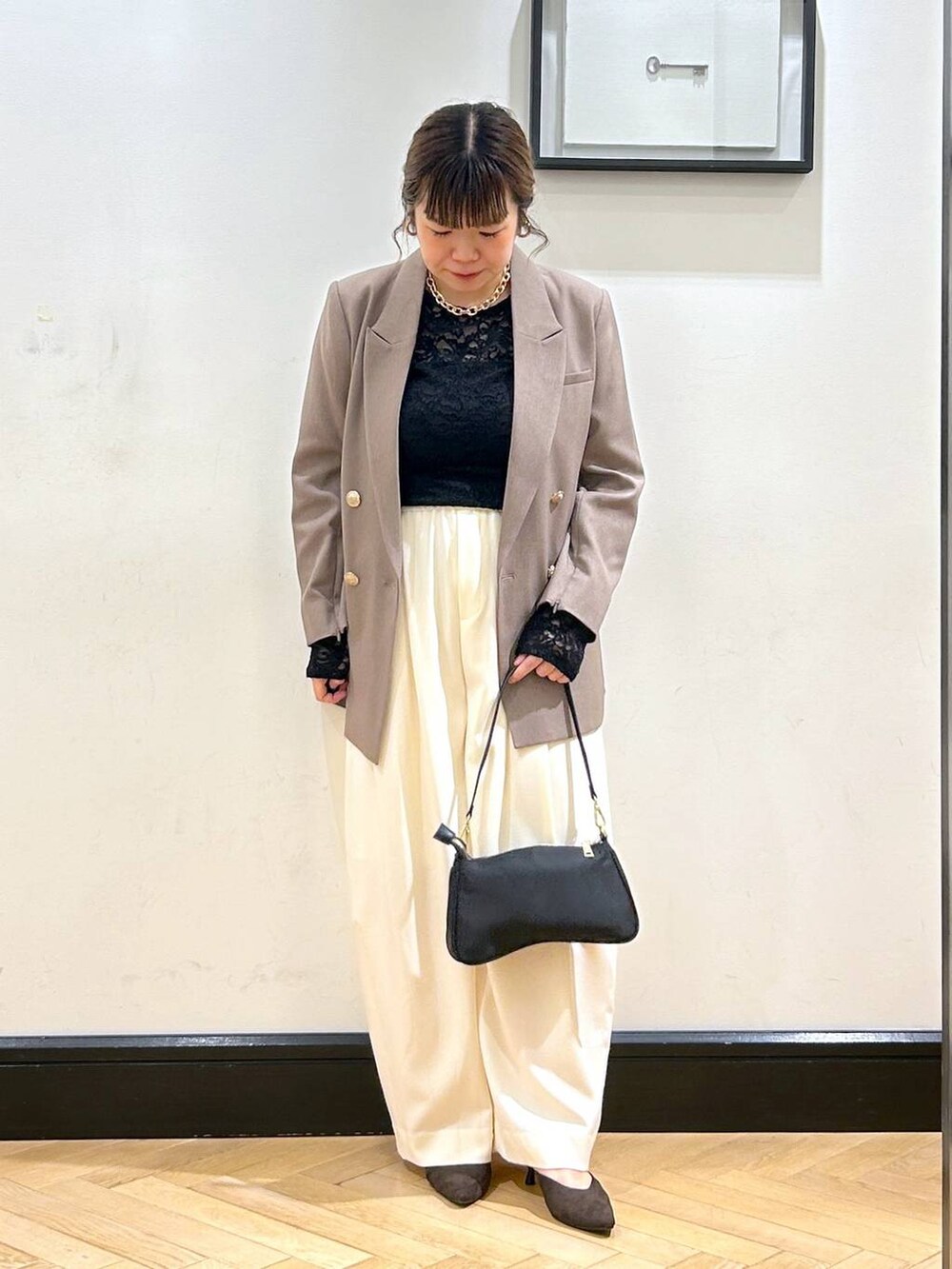 ホワイト系のスラックス、ブラウン系のパンプス、ブラック系のショルダーバッグを着用したレディースの秋コーディネートの2枚目の写真