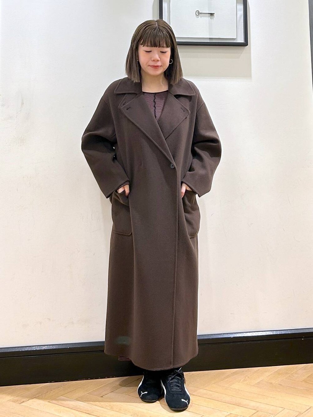 ブラウン系のステンカラーコート、ブラック系のスニーカー、ブラウン系のワンピースを着用したレディースの秋コーディネートの2枚目の写真