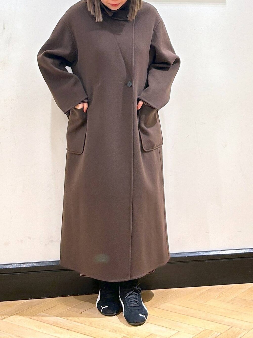 ブラウン系のステンカラーコート、ブラック系のスニーカー、ブラウン系のワンピースを着用したレディースの秋コーディネートの6枚目の写真