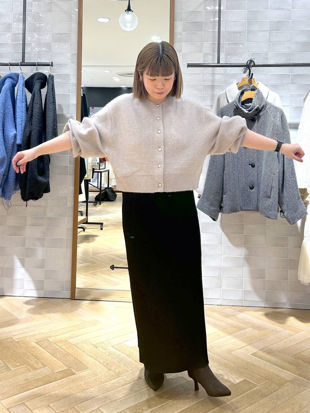 ブラック系のスカート、ベージュ系のカーディガン/ボレロ、ブラウン系のブーツを着用したレディースの秋コーディネートの2枚目の写真