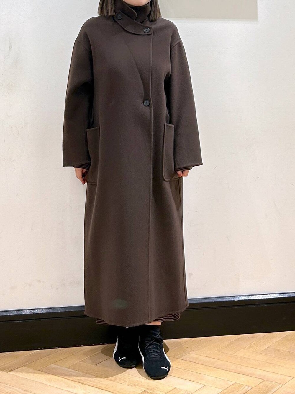 ブラウン系のステンカラーコート、ブラック系のスニーカー、ブラウン系のワンピースを着用したレディースの秋コーディネートの9枚目の写真