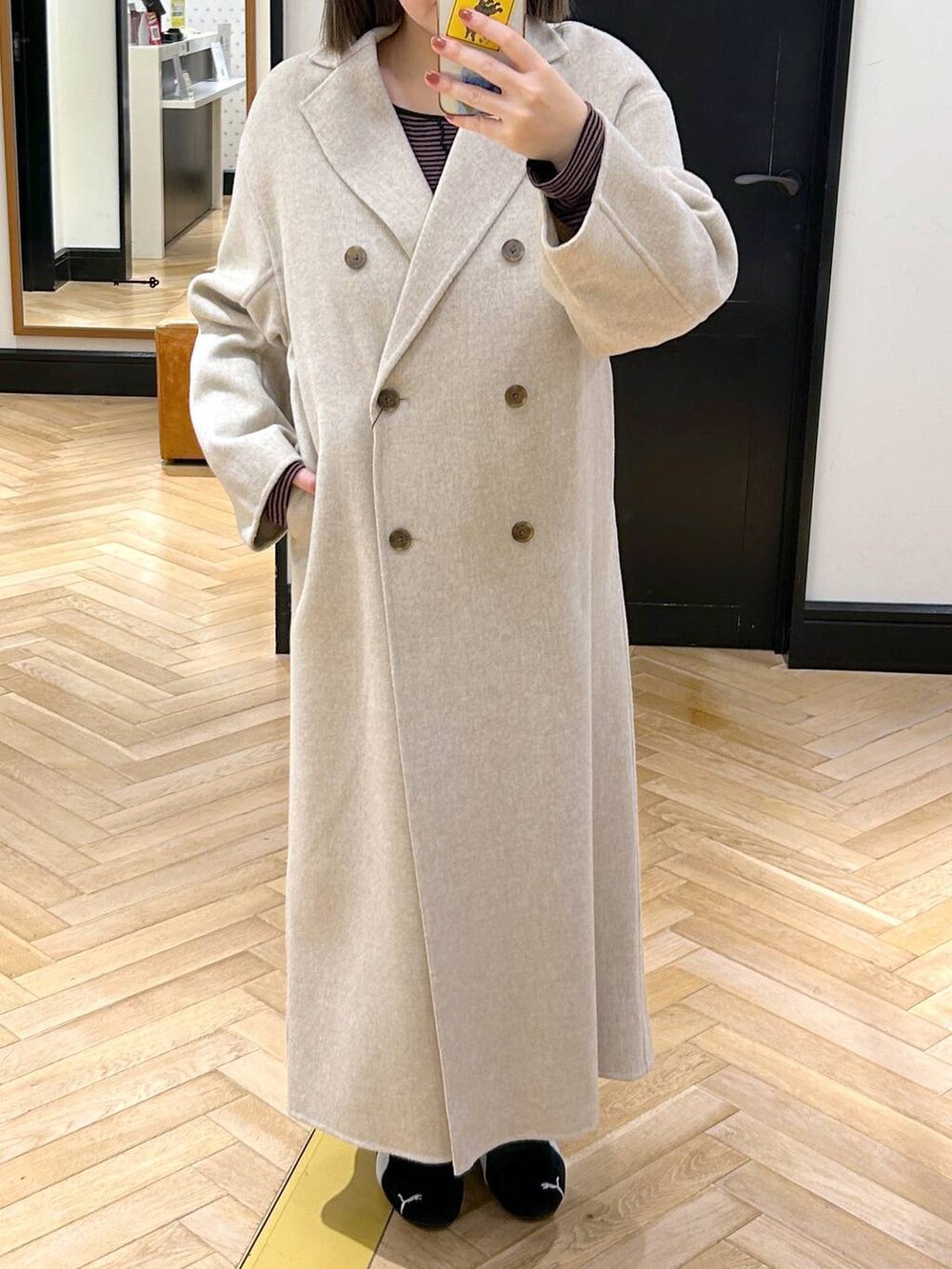 ベージュ系のチェスターコート、ブラック系のスニーカー、ブラウン系のワンピースを着用したレディースの秋コーディネートの2枚目の写真