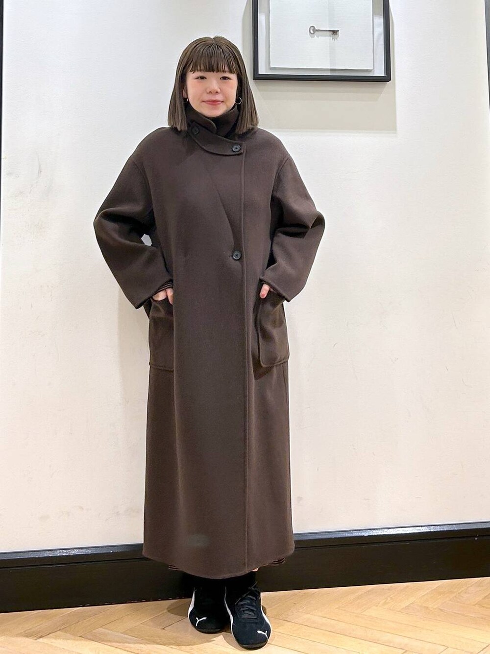 ブラウン系のステンカラーコート、ブラック系のスニーカー、ブラウン系のワンピースを着用したレディースの秋コーディネートの4枚目の写真