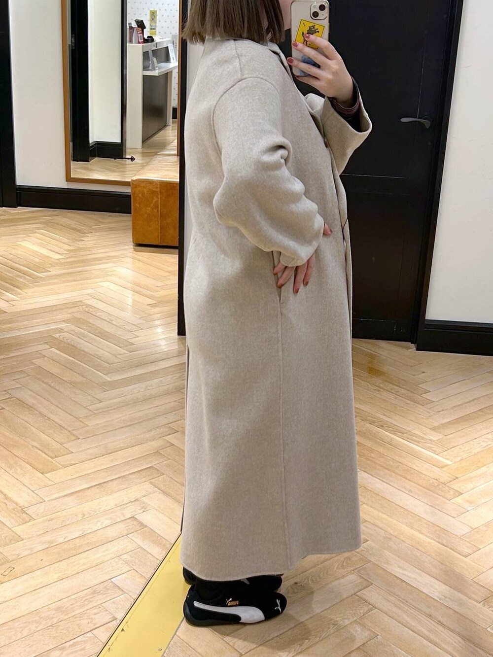 ベージュ系のチェスターコート、ブラック系のスニーカー、ブラウン系のワンピースを着用したレディースの秋コーディネートの3枚目の写真