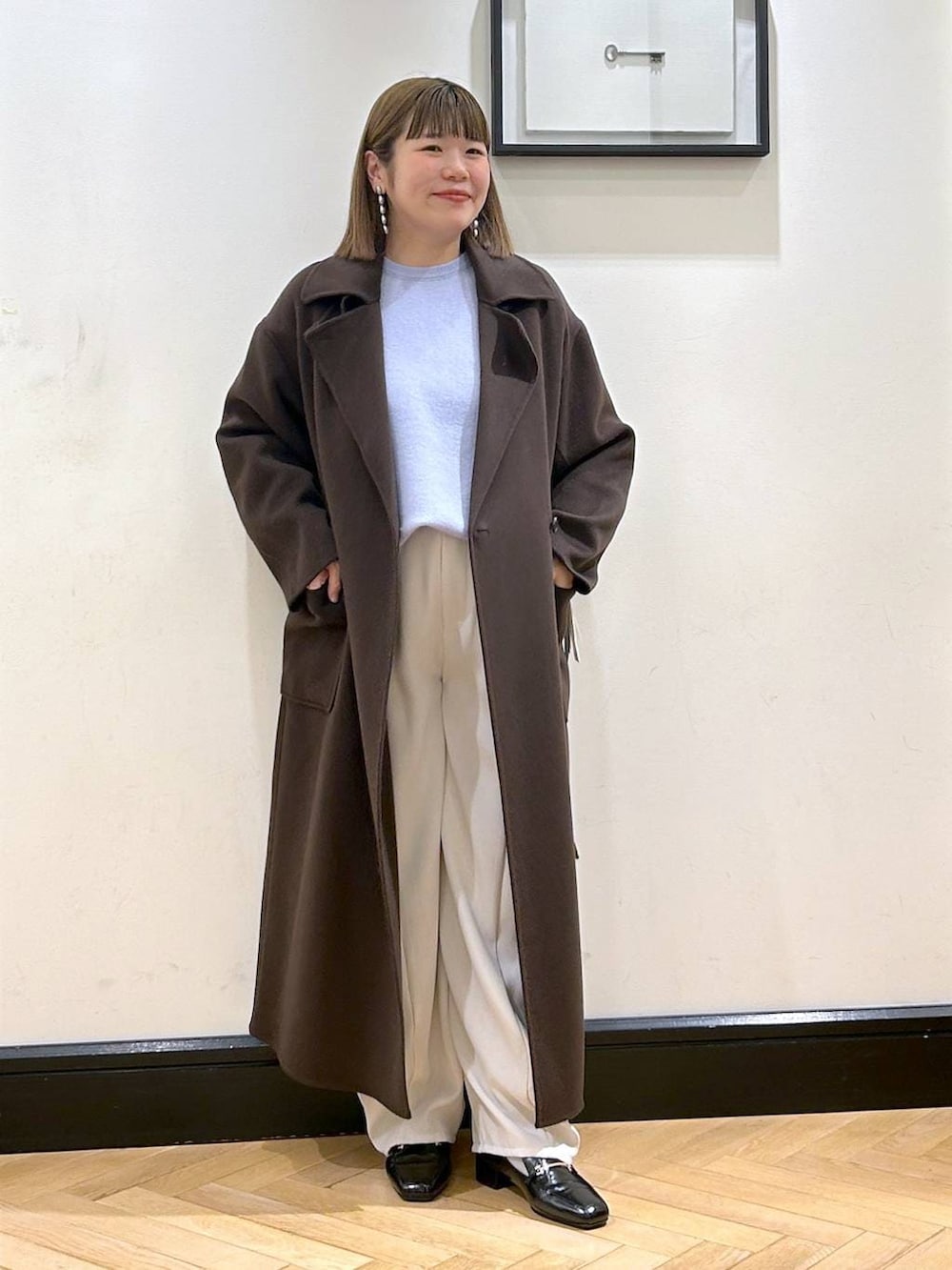 ブラウン系のステンカラーコート、ブラック系のローファー、ブルー系のニット/セーターを着用したレディースの秋コーディネートの2枚目の写真