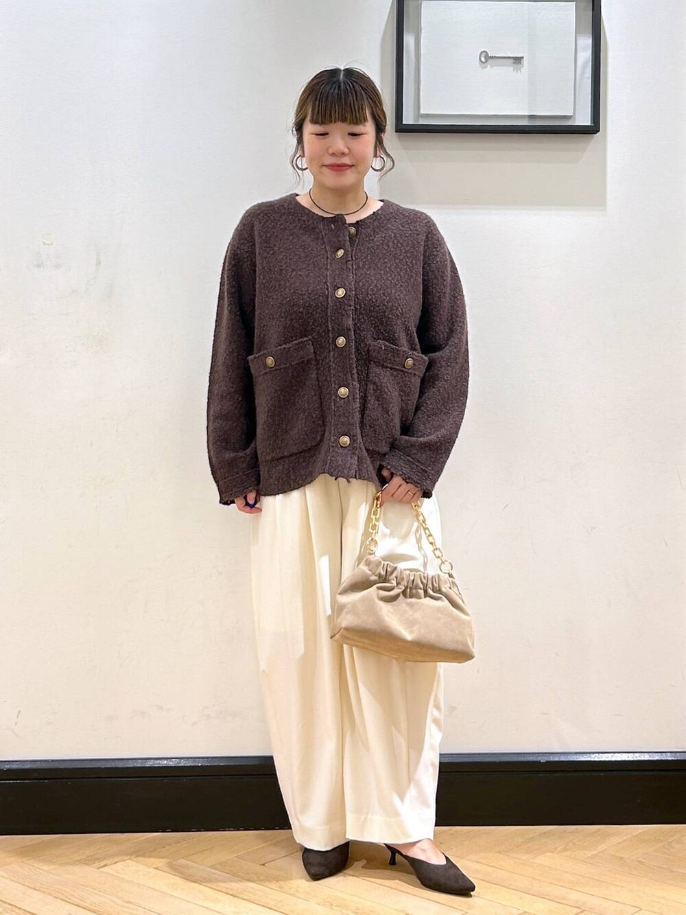 ホワイト系のスラックス、ブラウン系のパンプス、ベージュ系のショルダーバッグを着用したレディースの秋コーディネートの2枚目の写真