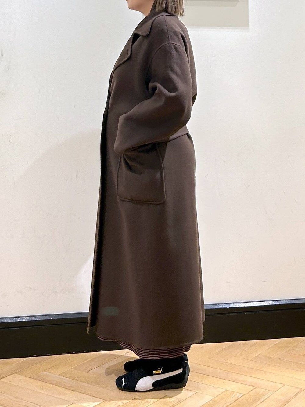 ブラウン系のステンカラーコート、ブラック系のスニーカー、ブラウン系のワンピースを着用したレディースの秋コーディネートの7枚目の写真