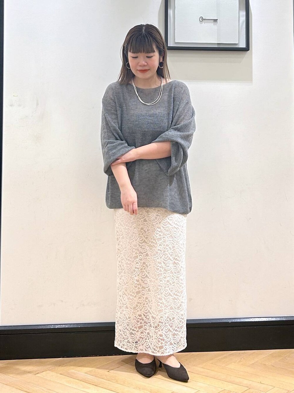 グレー系のニット/セーター、ブラウン系のパンプス、ホワイト系のスカートを着用したレディースの秋コーディネートの5枚目の写真