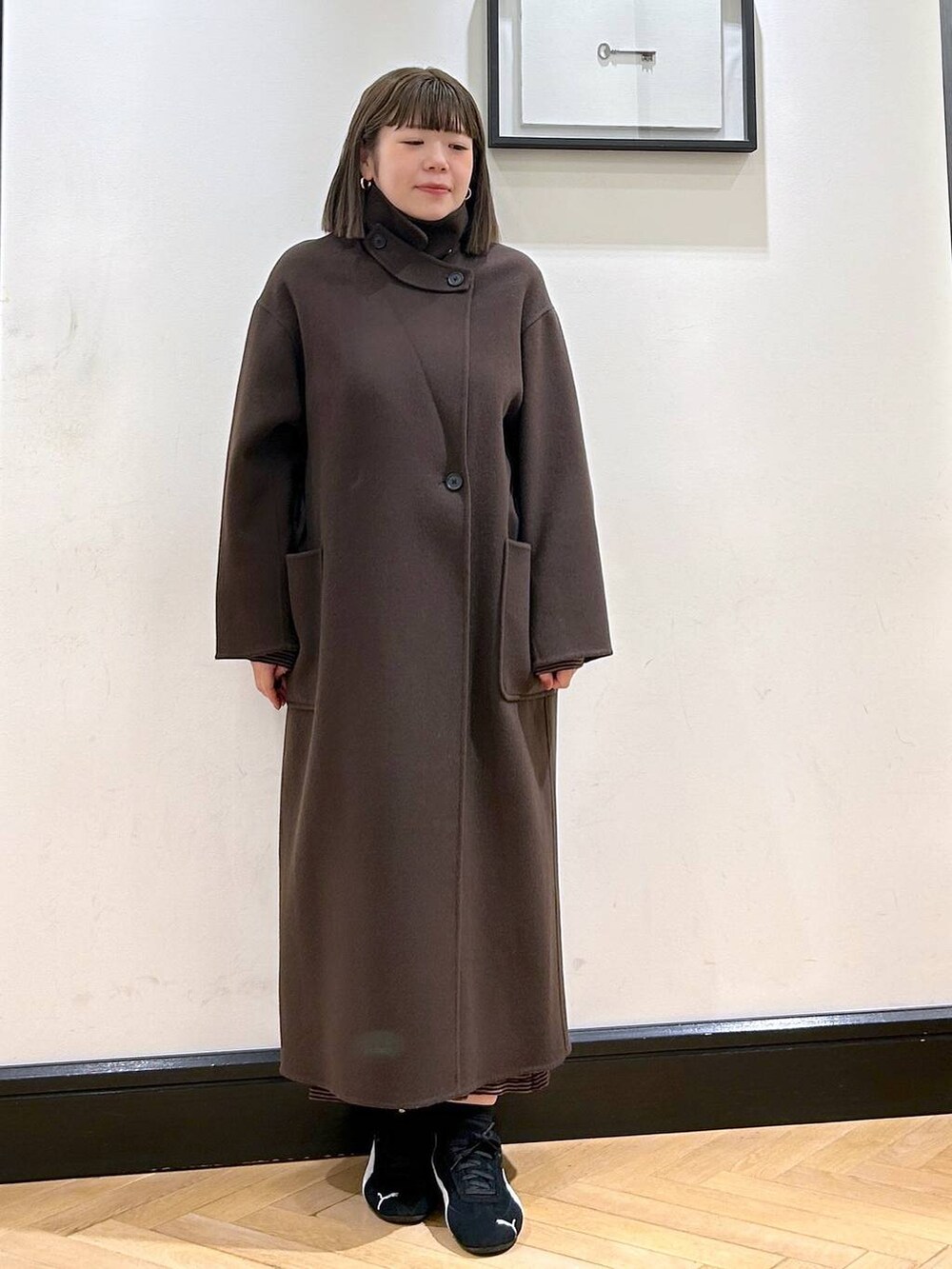 ブラウン系のステンカラーコート、ブラック系のスニーカー、ブラウン系のワンピースを着用したレディースの秋コーディネートの5枚目の写真