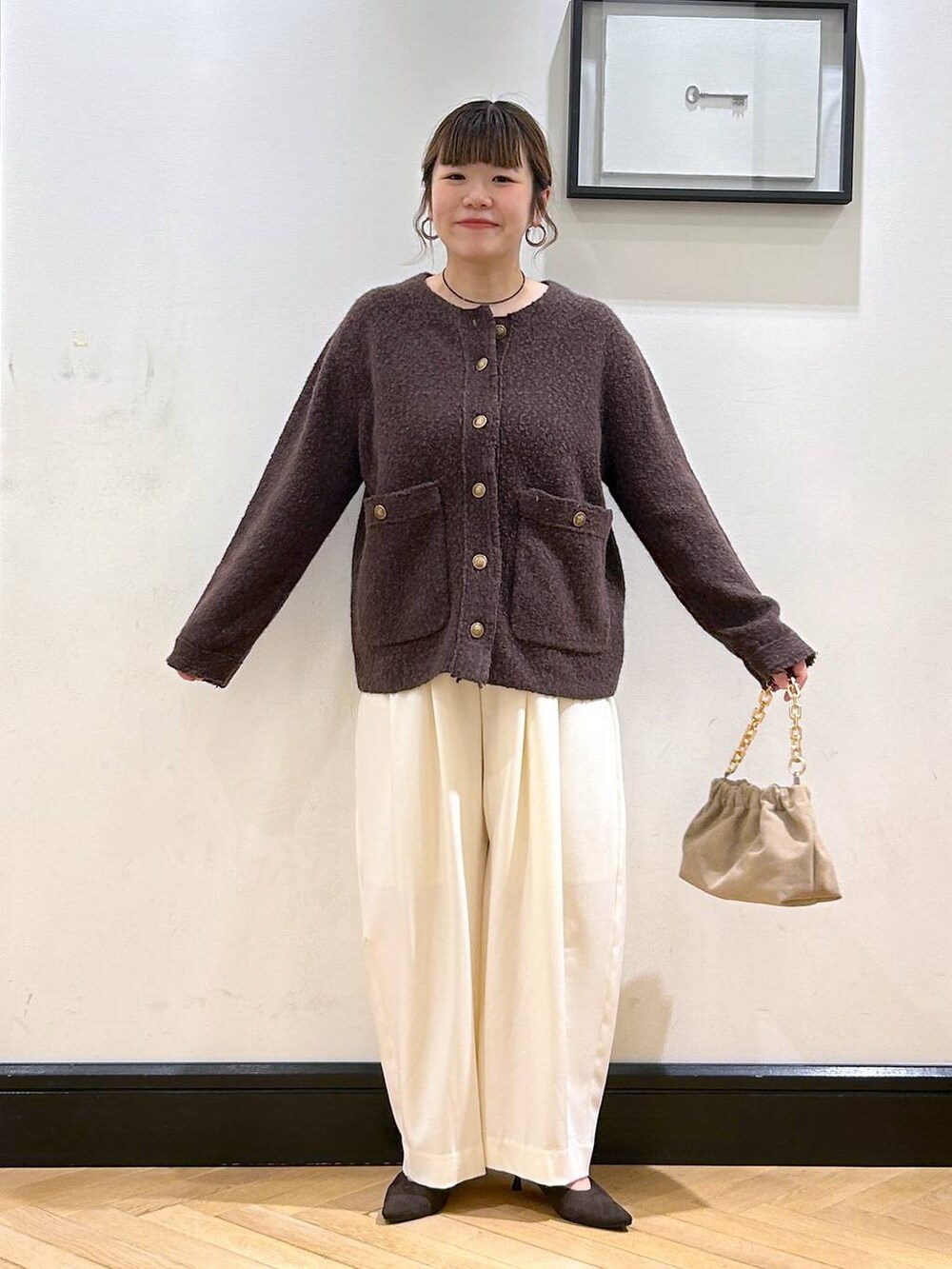 ホワイト系のスラックス、ブラウン系のパンプス、ベージュ系のショルダーバッグを着用したレディースの秋コーディネートの3枚目の写真