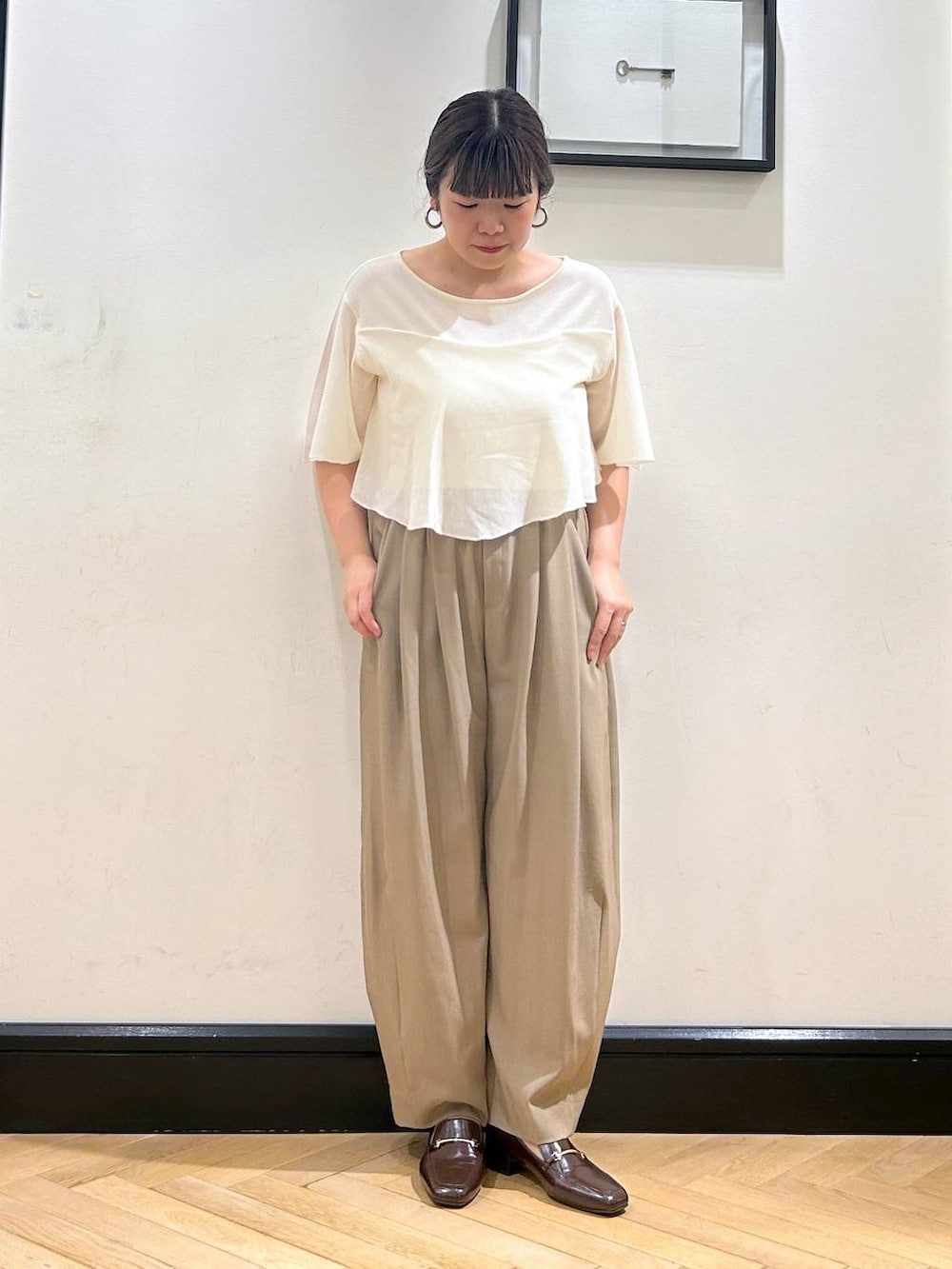 ベージュ系のスラックス、ブラウン系のローファー、ホワイト系のニット/セーターを着用したレディースの夏コーディネートの2枚目の写真