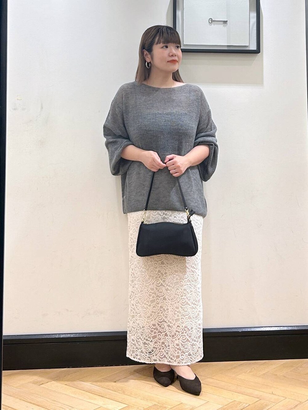 グレー系のニット/セーター、ブラウン系のパンプス、ホワイト系のスカートを着用したレディースの秋コーディネートの2枚目の写真