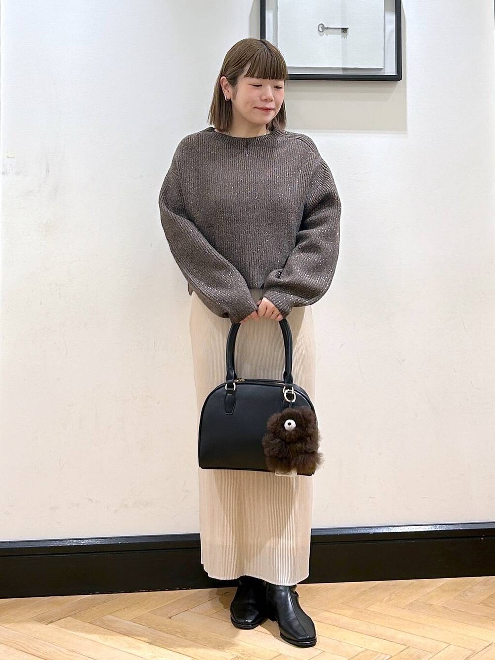 ブラウン系のニット/セーター、ホワイト系のスカート、ブラック系のブーツを着用したレディースの秋コーディネートの2枚目の写真