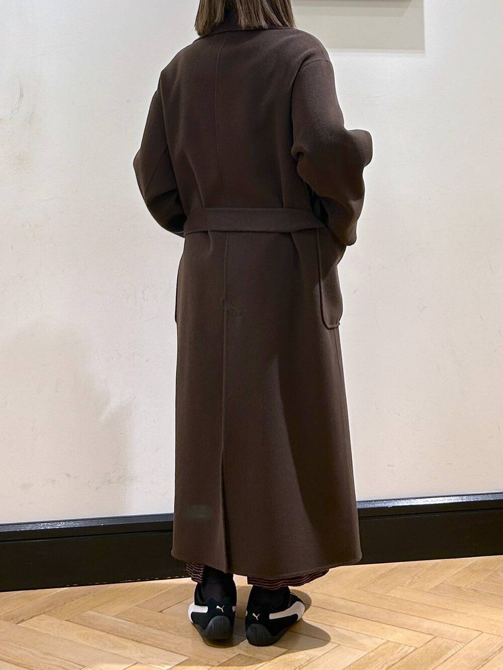 ブラウン系のステンカラーコート、ブラック系のスニーカー、ブラウン系のワンピースを着用したレディースの秋コーディネートの8枚目の写真