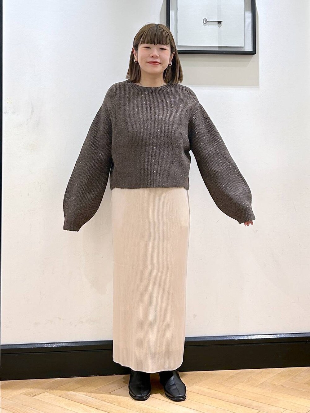 ブラウン系のニット/セーター、ホワイト系のスカート、ブラック系のブーツを着用したレディースの秋コーディネートの6枚目の写真