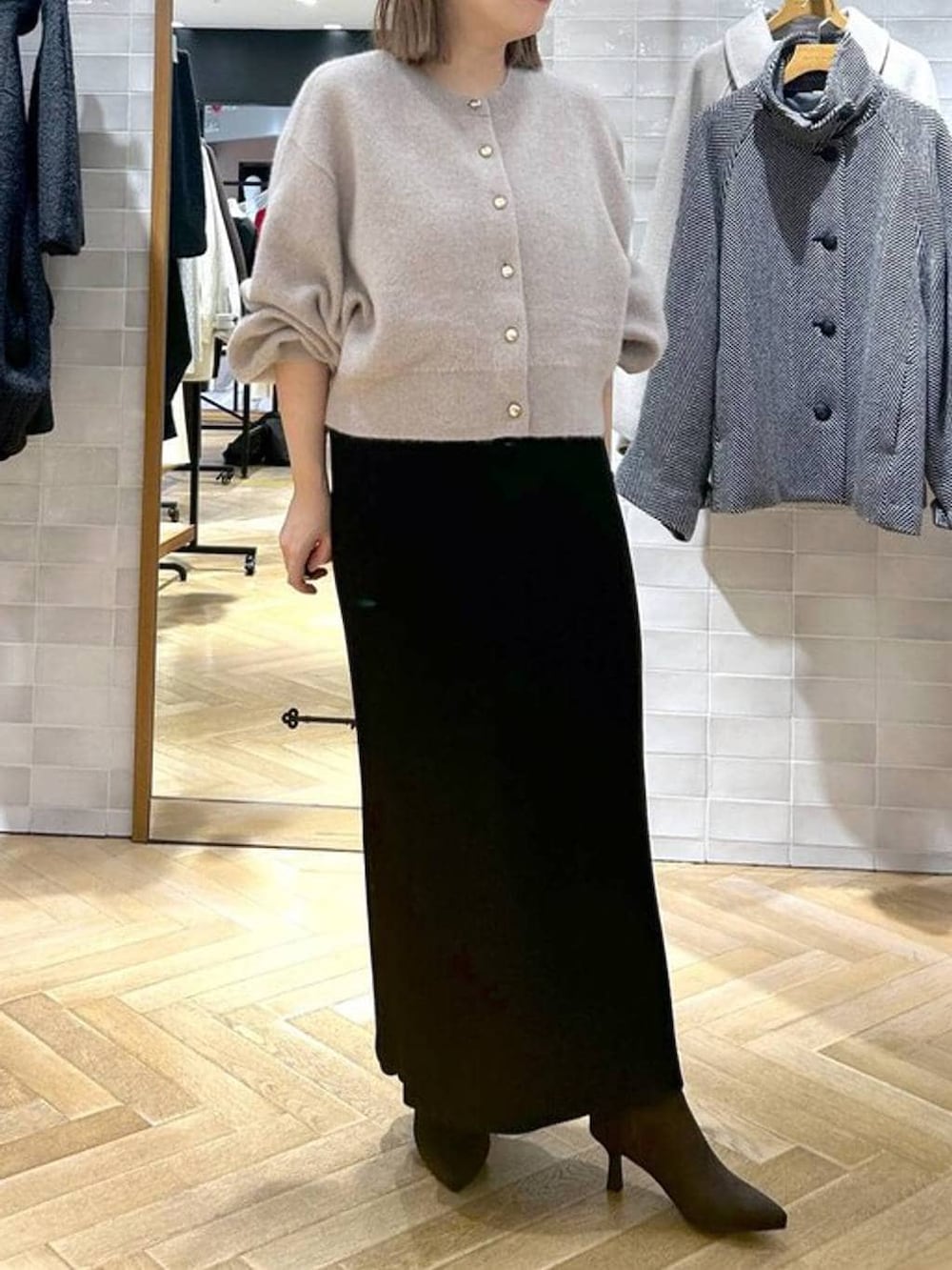 ブラック系のスカート、ベージュ系のカーディガン/ボレロ、ブラウン系のブーツを着用したレディースの秋コーディネートの3枚目の写真